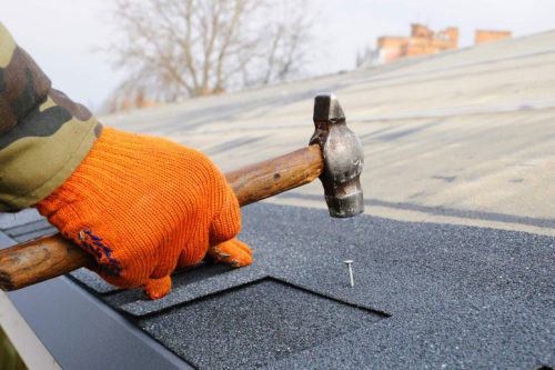man hammering roof shingles